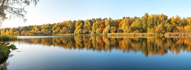 Panoramic view on lake with forest reflecting in calm water in Indian summer. Moscow, Russia.
