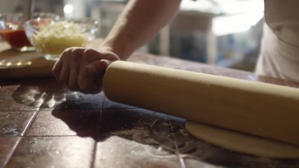 Tracking closeup shot in slow motion of hands of chef rolling dough on floury table in restaurant kitchen
