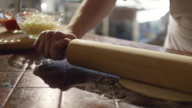 Tracking closeup shot in slow motion of hands of chef rolling dough on floury table in restaurant kitchen