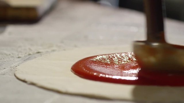 Tracking slow motion shot of applying tomato ketchup with metal ladle on pizza base