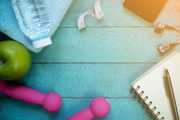 Notebook, nutrition food and fitness equipment on wooden background.