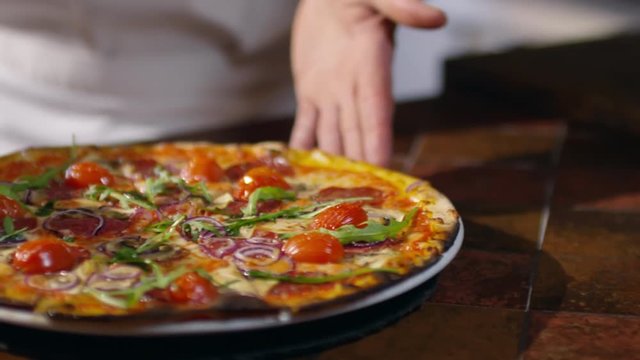 Tracking slow motion footage of hands of chef spinning plate with delicious freshly baked pizza on it