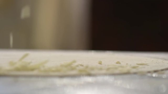 Tracking slow motion shot of putting shredded cheese over pizza crust