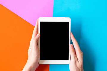Male hands holding tablet on colorful background.
