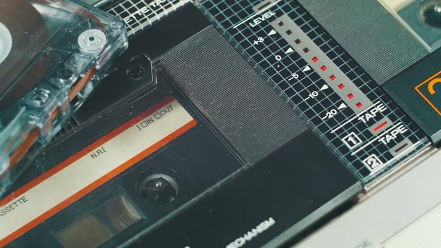 Playing an audio cassette in a tape recorder. Close-up. Black audio cassette with film rotates inside the deck. Red Record level indicator on a Vintage Cassette Deck.