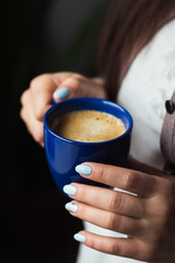 Girl with blue manicure holds a blue cup of coffee