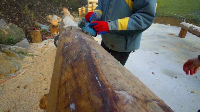 A man is slowly chiselling wood and making sure the outer surface of the tree trunk is flat and smooth enough.
