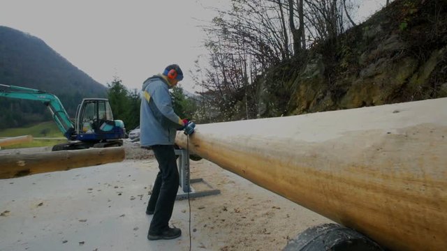 A man is chiselling wood and making sure the surface is flat enough. He is working outside.
