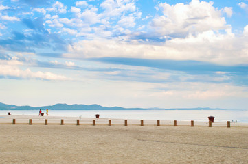 Stone tiles pavement near the sea shore against the background of a hill range and dramatic cloudy morning sky. Two women figures standing among birds on the shore. Zadar, Croatia