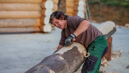 A young man is working really hard in order to peel off the skin on the tree trunk. He needs to be physically fit for this particular job.

