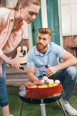 man and woman roasting meat and vegetables on barbecue grill