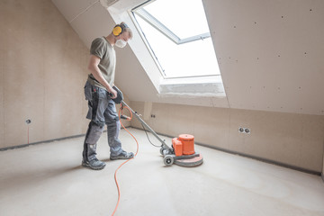 Handwerker schleift Estrichboden ab - 144945794