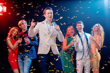 Carnival and party. Emcee with microphone. Group of cheerful friends toasting with wineglasses...