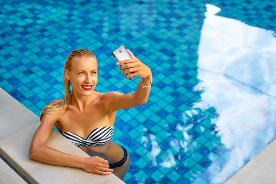 Vacation and technology. Pretty young woman using smartphone taking selfie in swimming pool.
