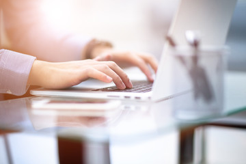 Young business man working on a laptop at his desk in the office, in view of the profile against the window