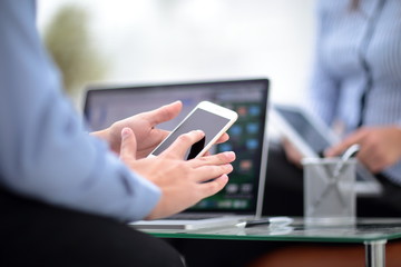 Texting to colleague. Confident young man in suit holding smart phone and looking at it while sitting at his working place