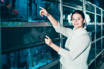 Girl in aquarium shop points to colored fish