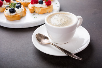 Cup of coffee with berry and goat cheese sandwiches on marble cutting board, top view, copy space.