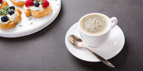 Cup of coffee with berry and goat cheese sandwiches on marble cutting board, top view, copy space.