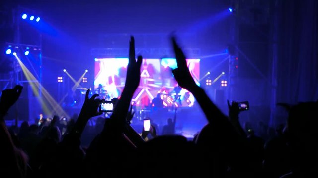 crowd partying at rock concert, hands up, cheering fans at live concert, crowd of people illuminated by colorful lights, tipsy fans dancing at open air performance, taking video at smartphone, show