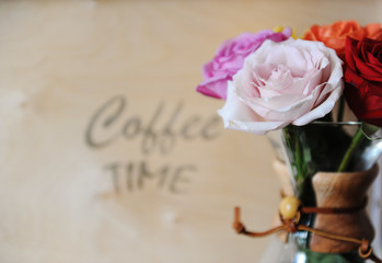 Colored roses in a coffee pot on a wooden background with an inscription coffee time