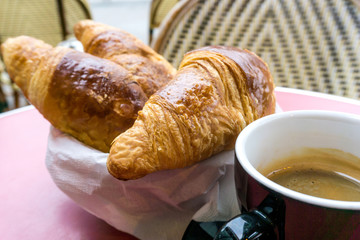 Breakfast with coffee and croissants in a basket on table