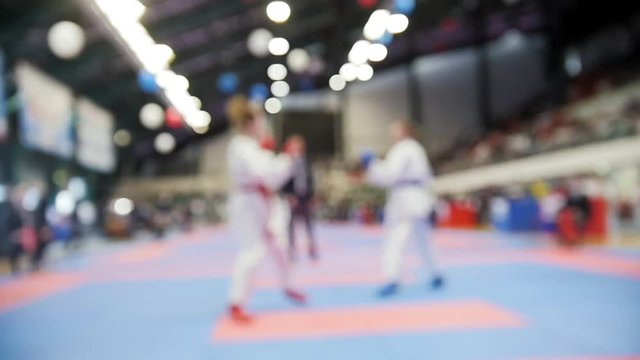 Kids karatekas fight on karate competitions, slow-motion de-focused sport background