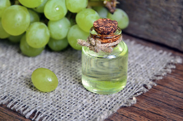 Grape seed oil in a glass jar and fresh grapes on old wooden table.Bottle of organic grape seed oil for spa and bodycare.Spa,Bio,Eco products concept.Soft selective focus.