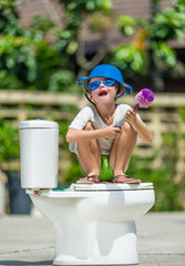 Absurd picture: cute boy in goggles sitting on the toilet, which is installed in the middle of the...