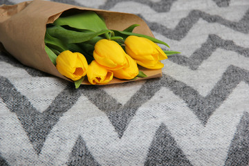 Spring bouquet of yellow flowers tulips laying on the grey blanket