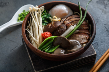 Ramen soup with duck and mushrooms over dark concrete background, close view