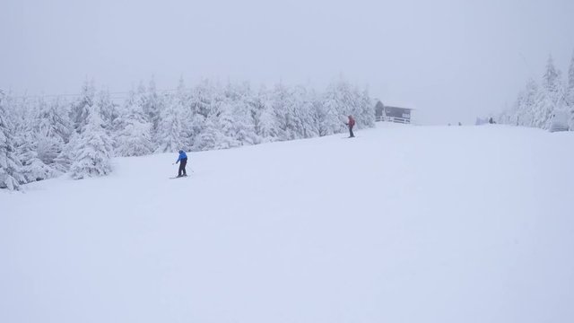 Terrible misty weather on slope in winter mountains. Few skiers down hill skiing. Winter mountain ski resort in terrible fog and snowing, skiers enjoying fresh powder snow on piste in mist and cold. 