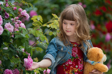 Young girl with teddy bear in the garden of wild rose