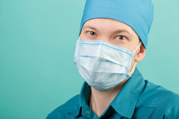 male surgeon in mask looking at camera on blue background, close up