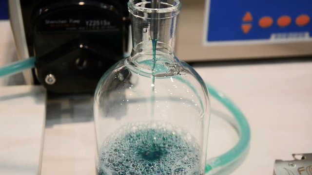 The liquid of blue color periodically pours out and drips from a thin metal tube