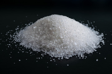Heap of granulated white sugar on black surface