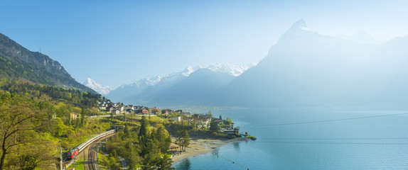 Small towns in Europe. Fluelen. Switzerland. View of the small town in the Alps mountains. Traditional houses. Railway along Lake Lucerne. Canton  Uri. - obrazy, fototapety, plakaty