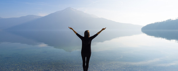 The joy of unity with nature. Woman with open arms by the lake on a background of mountains. - 144958350
