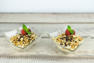 Zwei Schalen mit leckerem Dessert mit karamelisierten Mandeln, Schokostreuseln und frischen Himbeeren, Holzhintergrund und Textfreiraum