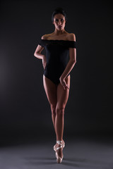 beautiful woman ballerina in black body suit posing on toes over black