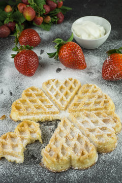 Eine frisch gebackenen Herzwaffel mit Puderzucker und frischen Erdbeeren und einem Sch&auml;lchen mit Sahne