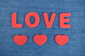 Das Wort Love in roten Buchstaben und drei rote Herzen auf blauem Jeansstoff