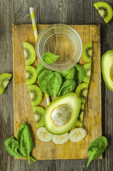 The concept of detox drink, ingredients (spinach, avocado and banana) are laid out in the form of a glass of cocktail on a wooden board on a black wooden background
