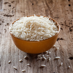 Uncooked dry rice in brown bowl on wooden table