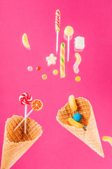 waffle cones with different delicious jelly candies and lollipops on pink