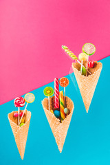 waffle cones with different delicious jelly candies and lollipops on blue and pink