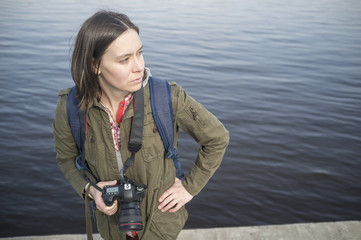 Obraz premium Pensive woman photographer with camera in hand standing on the background of the river and looks into the distance.