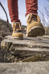 Girl walks along the old rotten wooden bridge in stylish boots, on a spring sunny afternoon.