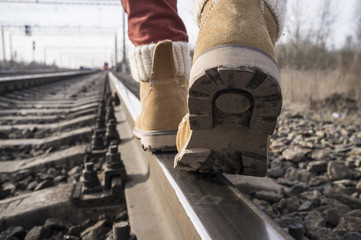 Legs in stylish boots go on rails on the railway, against the background of the approaching train. Close-up.