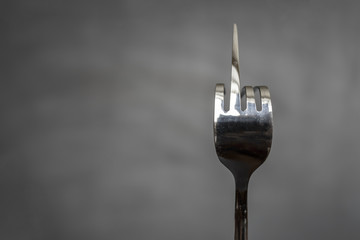 Fork bent in the form of an obscene gesture sign of the middle finger on a blurred gray background